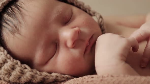 Newborn baby sleeping peacefully with checkered cloth on brown background alt