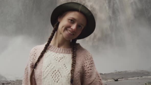 Happy woman traveler with pigtails and hat go to camera, smiles near waterfall Karakaya-Su, holidays