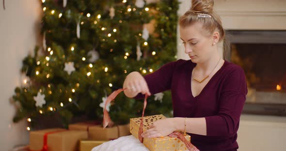 Young Woman Tying Ribbon On Christmas Present alt