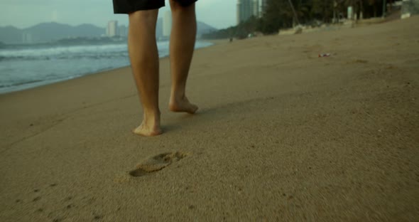 Closeup of the Legs of a Young Caucasian Man Walking on the Sand Along the Shore Outdoors Against alt