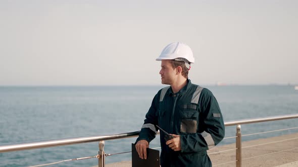 Port Inspector in Helmet and Coverall Filling Vessel Inspection Checklist During Control Inspection alt