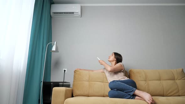 Brunette Woman Turns on the Air Conditioner While Sitting on the Couch alt