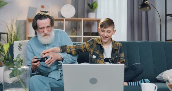 Bearded Retired Granddad and His Grandson Enjoying Video Games on Laptop alt