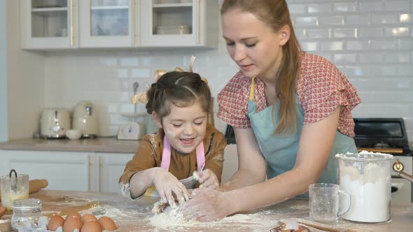 Happy Mother and Daughter Cook Together in the Kitchen, Knead the Dough. The Daughter Laughs and alt