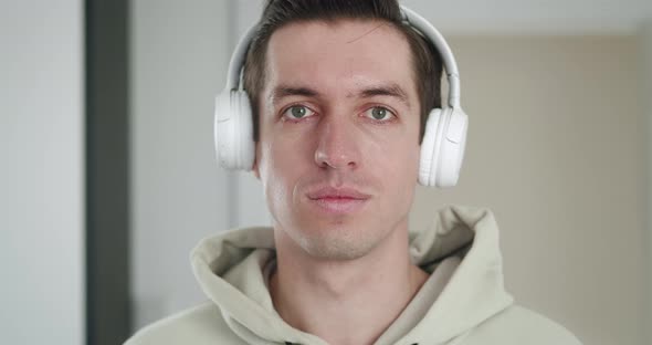Portrait of a Stylish Man in White Headphones Listening to Music and Looking at the Camera Indoors alt