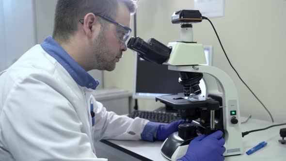 Bearded Caucasian Male Researcher Wearing Protective Glasses and Working with a Microscope Spbas alt