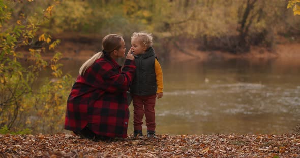 Woman Is Playing with Her Toddler in Forest, Resting on Shore of Lake at Autumn Day, Happy Family alt