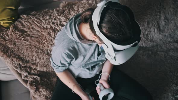 Young Woman in Virtual Reality Helmet Sitting on Sofa and Move Hands at Home alt