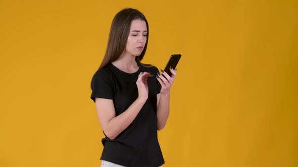 young girl using smart phone and texting online chat isolated on yellow background