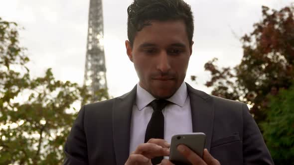 Businessman in a Suit Looks at His Phone on the Background of the Eiffel Tower alt