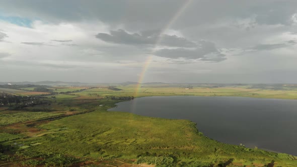 Aerial shot flying over swampland towards a rainbow over lake Victoria. alt