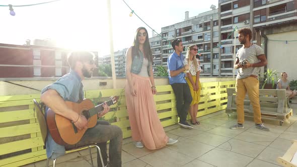 Friends having fun on the rooftop terrace, playing guitar and taking photos alt