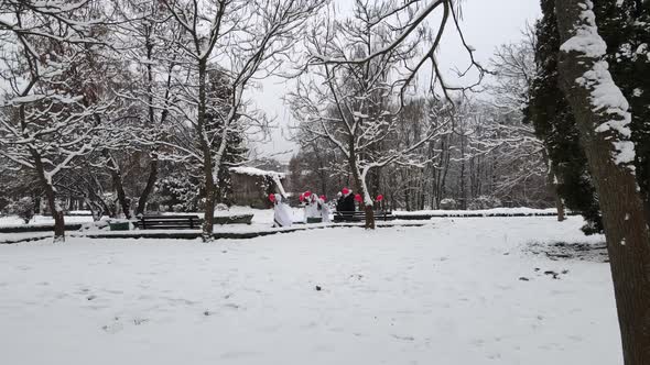 Boys And Girls Run Through A Snowy Park With Heart Shaped Balloons