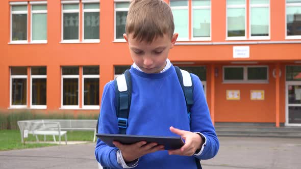 A Young Boy Works on a Tablet in Front of an Elementary School alt