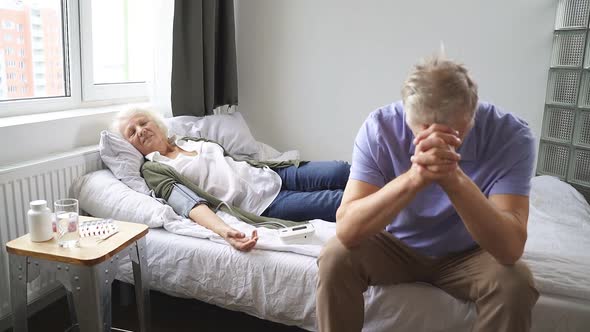 Mature Woman Sleeps on the Bed and the Husband Sits Next To Her and Worries About His Wife Because alt