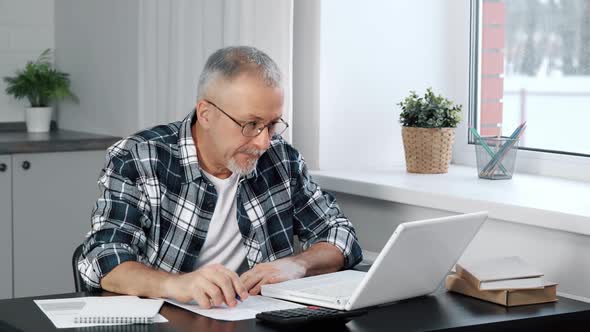 A Happy Elderly Man Enjoys the Good News While Looking at His Laptop