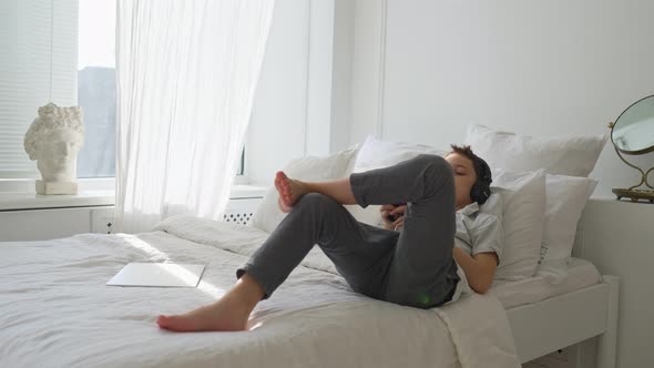 11 Years Old Boy Lies on the Bed and Listens to Music with Headphones alt