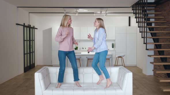 Happy Family Senior Mom Having Fun with Adult Daughter Dancing on Sofa in Living Room alt