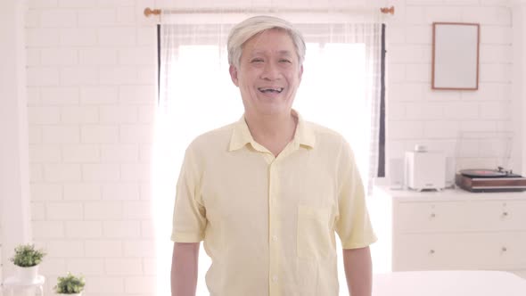 Asian elderly man feeling happy smiling and looking to camera while relax on the sofa. alt