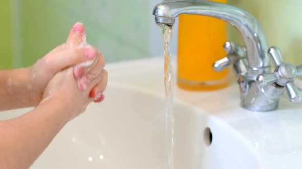 child washes his hands with soap with a bath