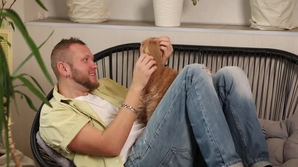 Man lying on the sofa holding cute ginger cat, male hugging her cute kitty