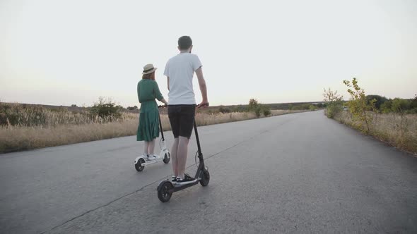 Happy Couple Riding on Electric Scooters Into the Distance and Having Fun on Way alt