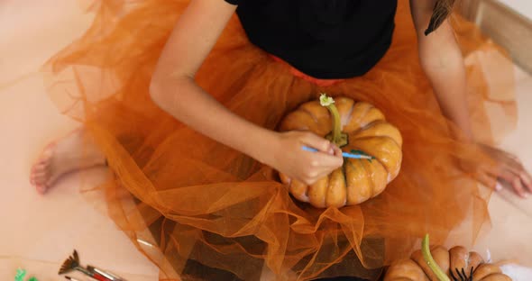Happy child decorating a pumpkin at home Little girl drawing face on orange Halloween