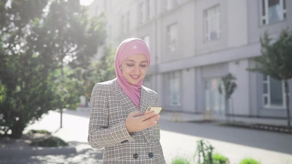 Young Beautiful Muslim Woman Wearing Hijab Headscarf Walking in the City Using Smartphone