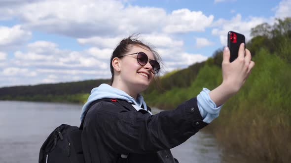 Woman Stands on the Pier of the River Takes a Selfie on the Phone Smiles Happy