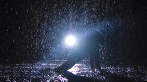 A Woman Is Silhouetted Under Streams of Rain Who Is Doing the Exercise Lunges. Dark Studio and alt