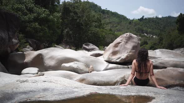 Lady sits on huge river polished rock against forestry hill