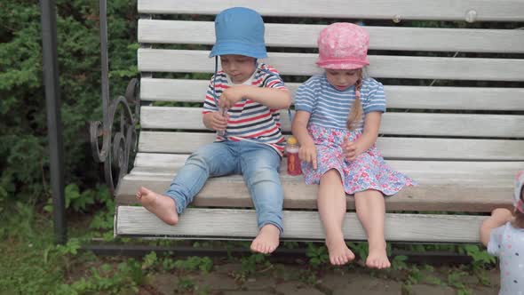 Happy Children on Garden Swing Bench Blowing Soap Bubbles