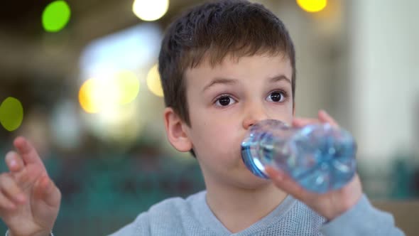 Boy Drinking From Plastic Bottle of Water in Fast Food Restaurant
