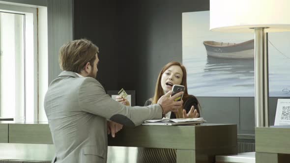 Businessman using credit card and smartphone to check in at hotel reception alt