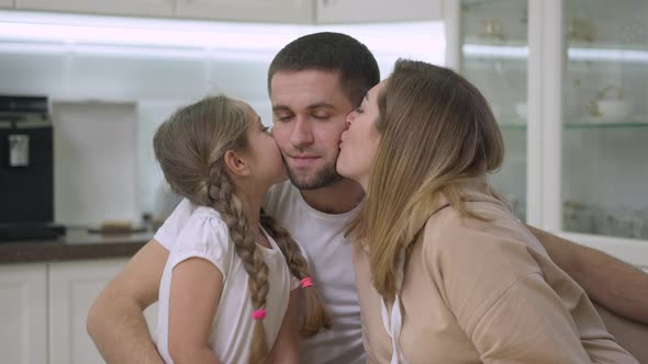 Wife and Daughter Kissing Man on Cheeks Looking at Camera and Smiling alt
