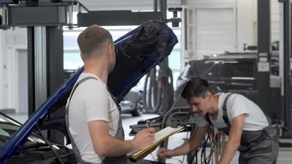 Two Mechanics Discuss Repairing Broken Automobile at the Garage