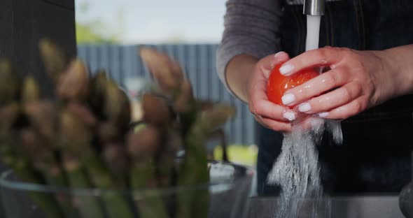 A Woman Washes Tomatoes in the Foreground of a Bowl of Asparagus alt
