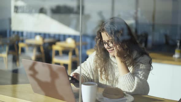 Freelancer Works on Laptop Near Window in Cafe