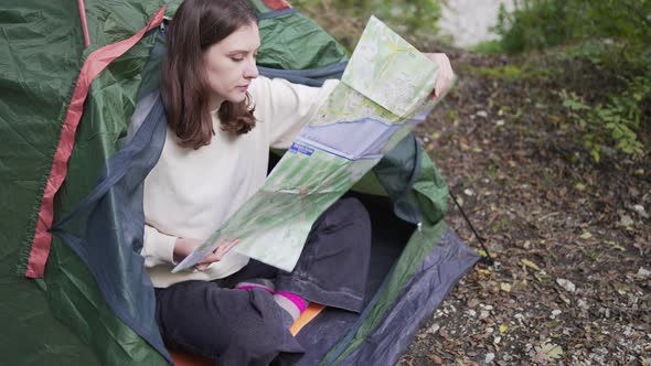 A Woman Reads a Map in a Tent in the Woods