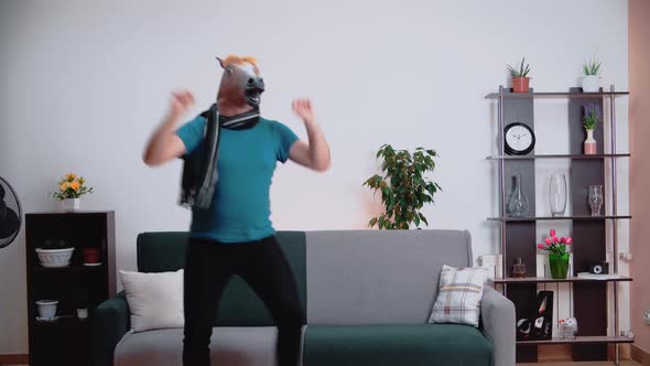 In the room, a man dances in a horse mask, spreading his arms to the sides alt