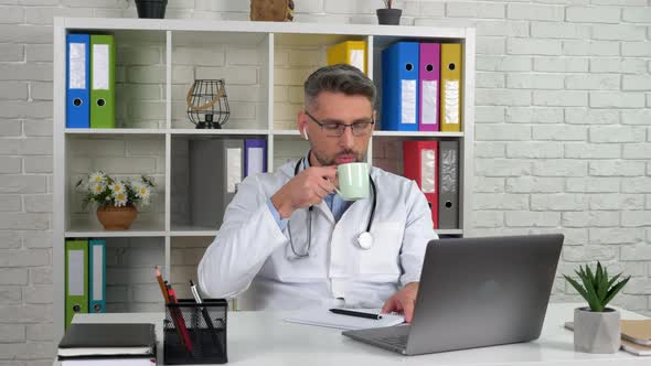 Doctor listens patient online video call laptop webcam, drinking coffee tea alt