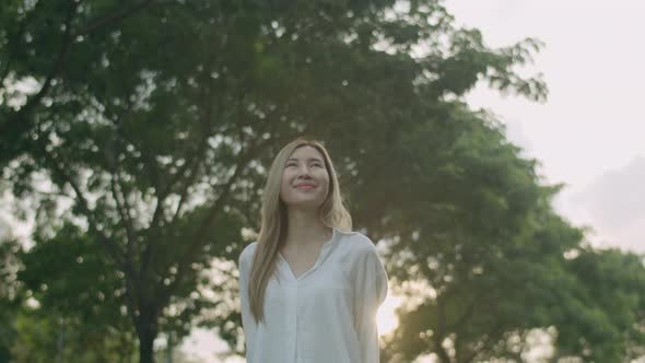 Asian woman looking around her enjoying the breeze in the public park.