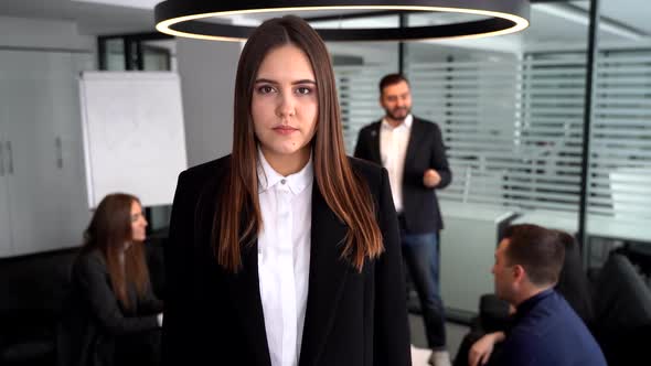Businesswoman in Modern Open Plan Office Work Space Smiling Into Camera with Colleagues in
