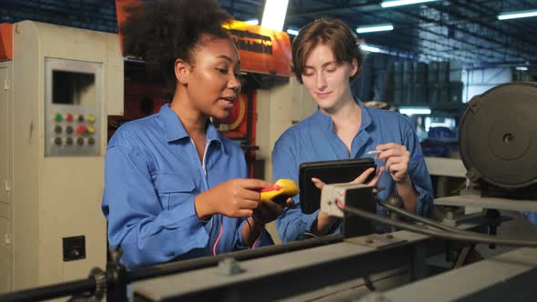 Two professional female engineers inspect machines' electric systems at factory. alt