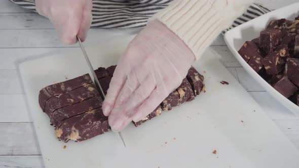 Step by step. Cutting homemade macadamia fudge on a white cutting board. alt