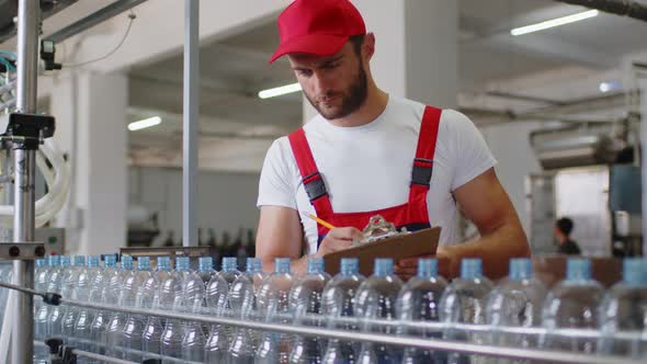 Young Factory Man in Uniform Making Notes on Clipboard at Water Production Factory