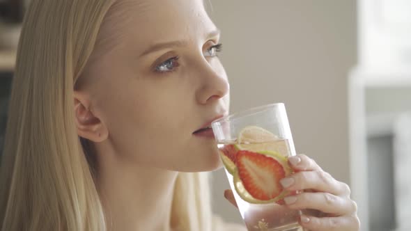 Happy Young Blonde Girl Drinks Water with Lime and Strawberry alt