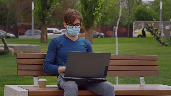 Young professional freelancer man wearing a surgical face mask, working on laptop alt