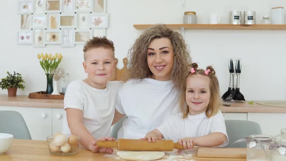 Son Daughter and Mother Look at the Camera While Rolling Out the Dough Together in the Kitchen alt
