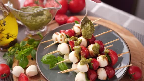 Pouring Pesto Sauce on Caprese Canapes with Cherry Tomatoes and Mozzarella Cheese Balls alt